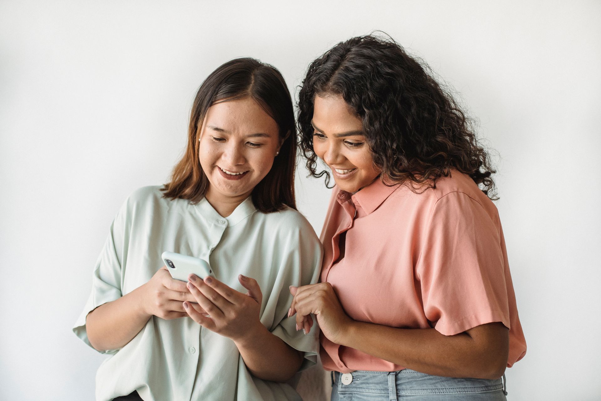 Two friends standing together and smiling as they look at an invitation on a phone screen